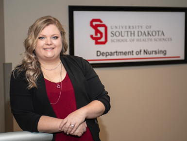 Ashley Herrity leans on a counter in front of a University of South Dakota Department of Nursing sign.