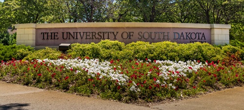 The University of South Dakota street sign, with red and white flowered landscaping in full bloom