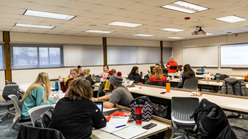College education students sit at tables in a classroom and learn. 
