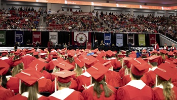 USD Class of 2023 graduates sit together in caps and gowns.