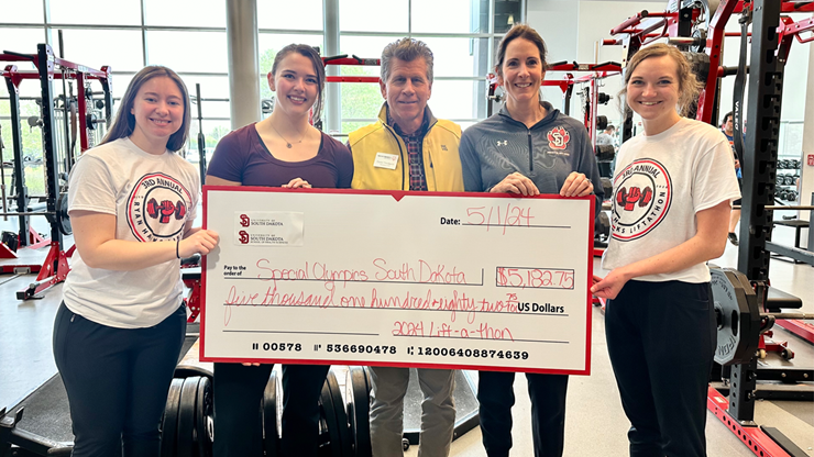 Five people stand together in the USD Wellness Center and hold a large check for Special Olympics South Dakota.