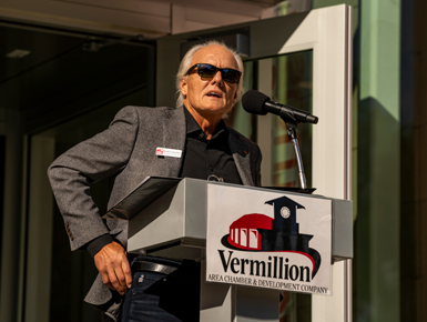 A photo of Scott Lawrence speaking at a podium in front of the National Music Museum in Vermillion.