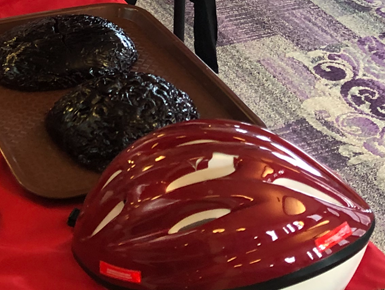 A bike helmet sits on a table next to two human-sized gelatin brains.