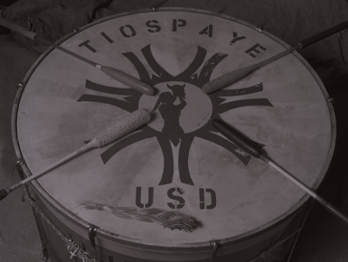 A grayscale image of a drum that says Tiospaye USD on it. 