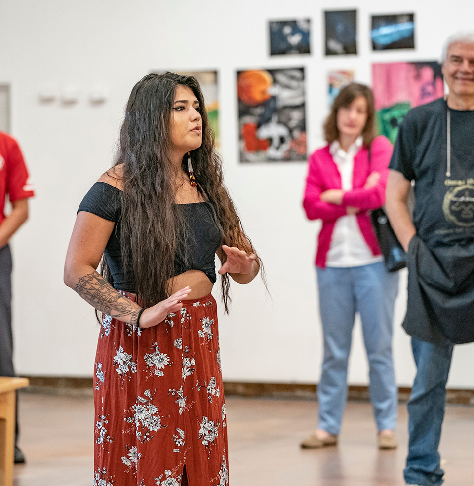 A USD art student showcasing her gallery to a small crowd.