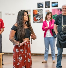 A USD art student showcasing her gallery to a small crowd.