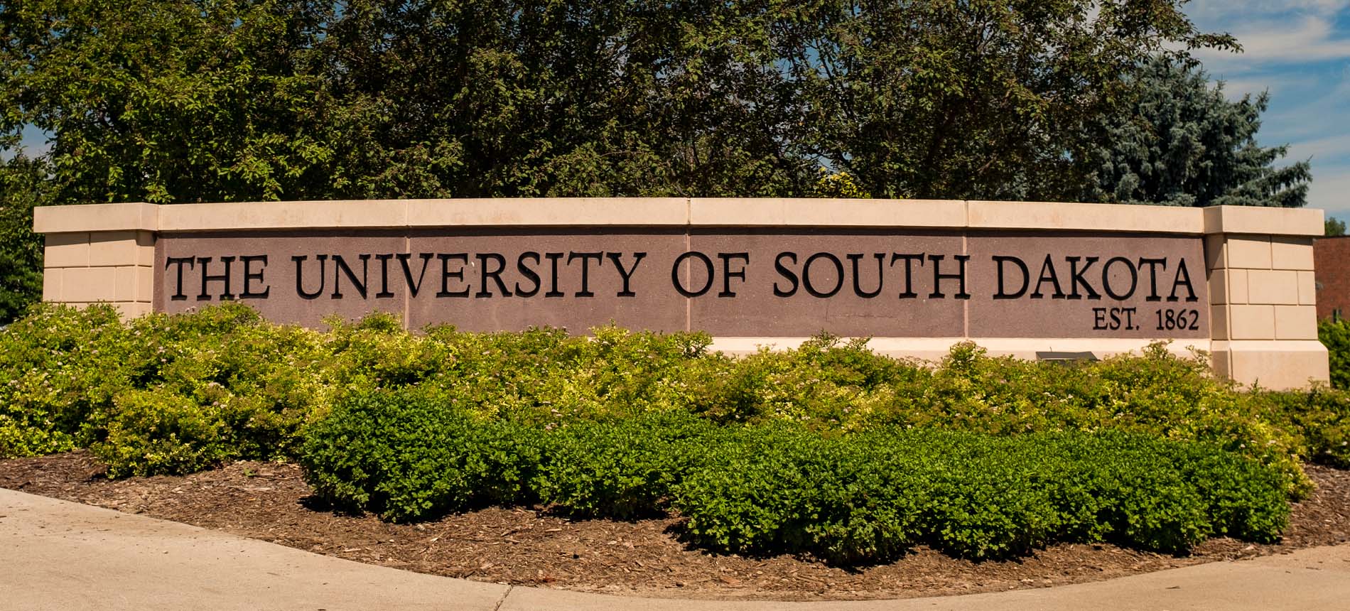 University of South Dakota Sign Behind Shrubs.