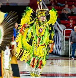 A student participating in the Native Wacipi event, wearing a bright green and yellow outfit.