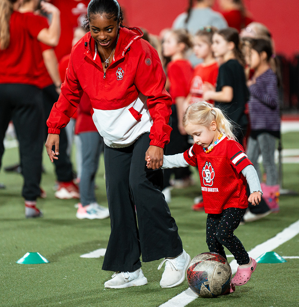 USD Soccer Player holds hand with child while kicking a ball