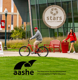 A student riding a Green Initiative Fund bike in front of the MUC. A bronze icon says Stars, a program of a a she bronze. Another says aashe.
