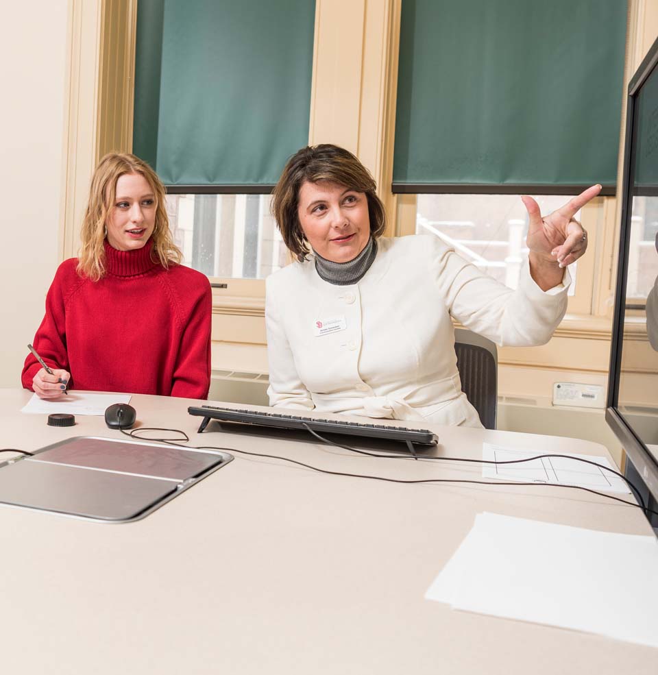 Student and professor sitting at a table while looking at a screen and discussing