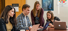 students looking at a laptop having a discussion with their professor