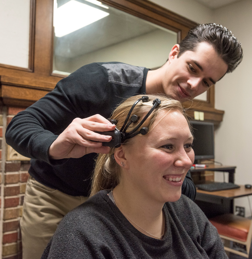 A student connecting a psychology device to another's head.