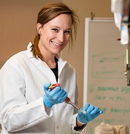 Student wearing gloves and lab coat working with lab equipment.