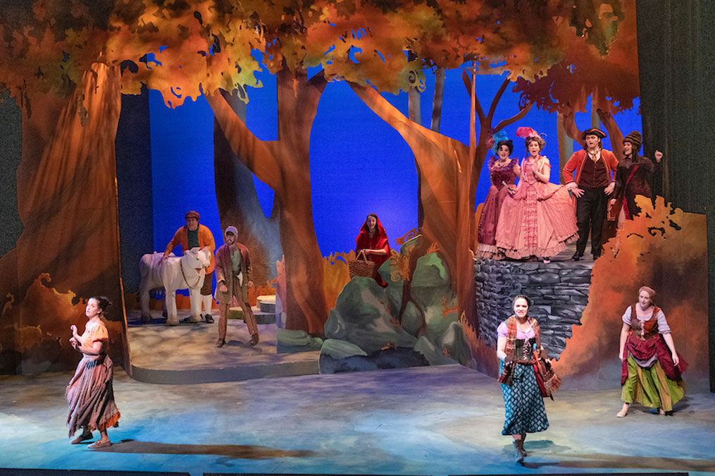 Theatre production with actors on stage decorated as if under trees in the evening