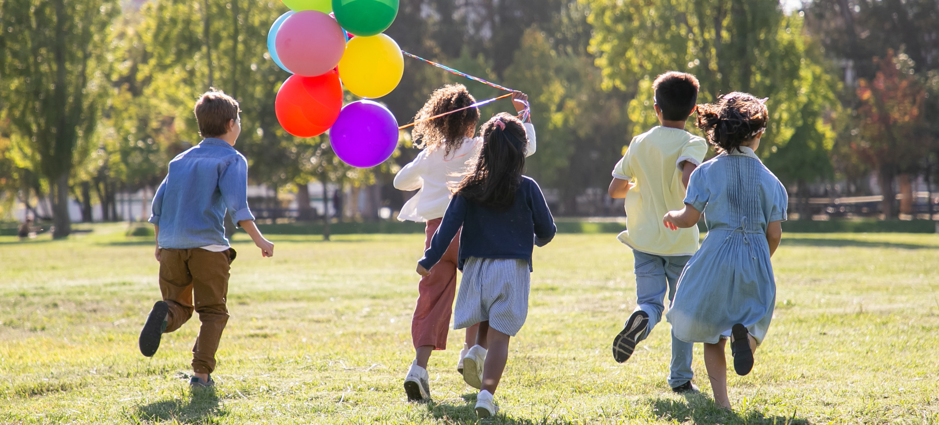 Five children holding balloons running in a field.