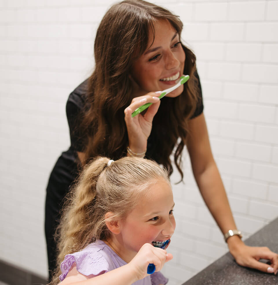 a student and child brushing their teeth in a mirror