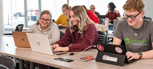 Three social work students on their laptops in the classroom.