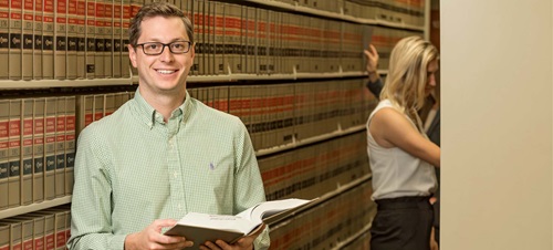 A male student in the law library smiling holding a book.