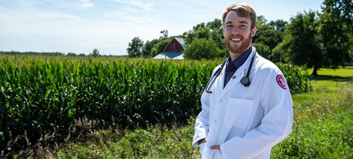 Male in White Lab Coat Standing by Corn Field.