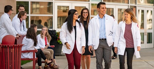 Group of Medical Students in White Coats Walking Outside of Building