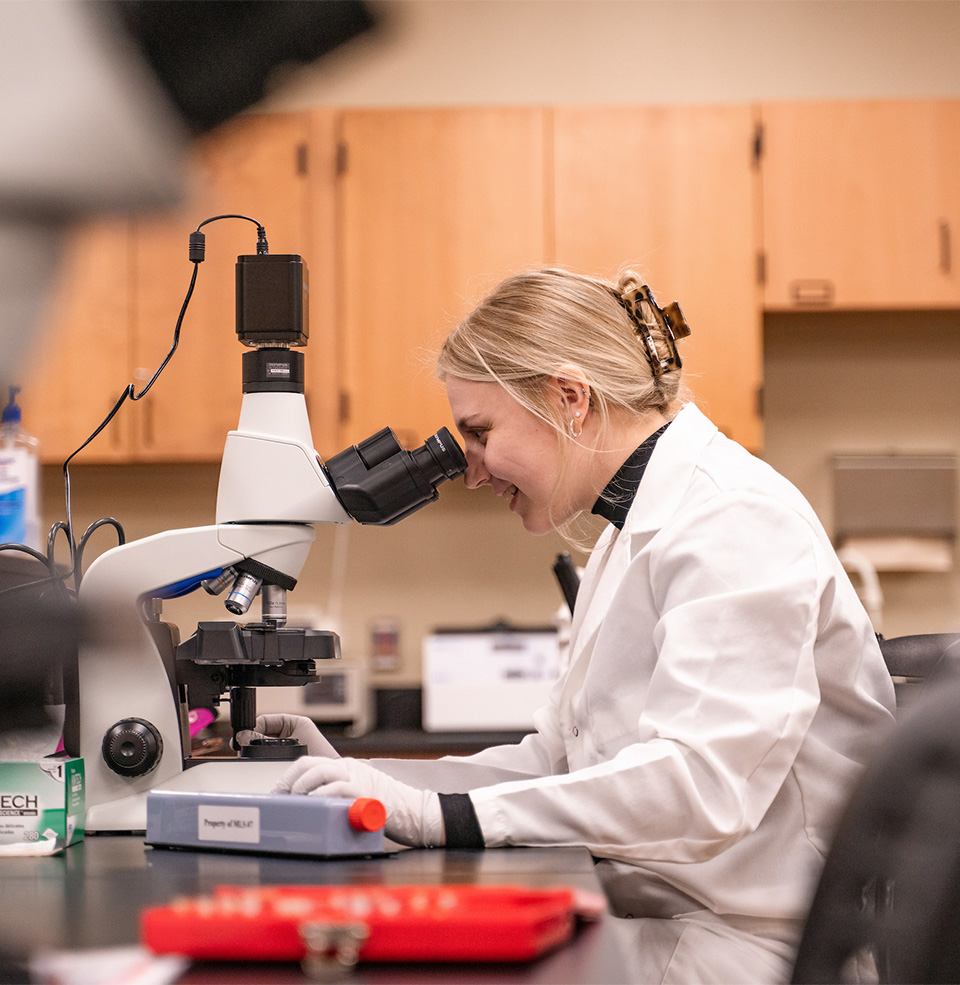 A student in the med lab looking into a microscope.