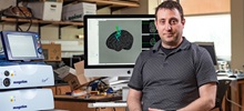 Lee Baugh smiling in front of a monitor showing brain research.