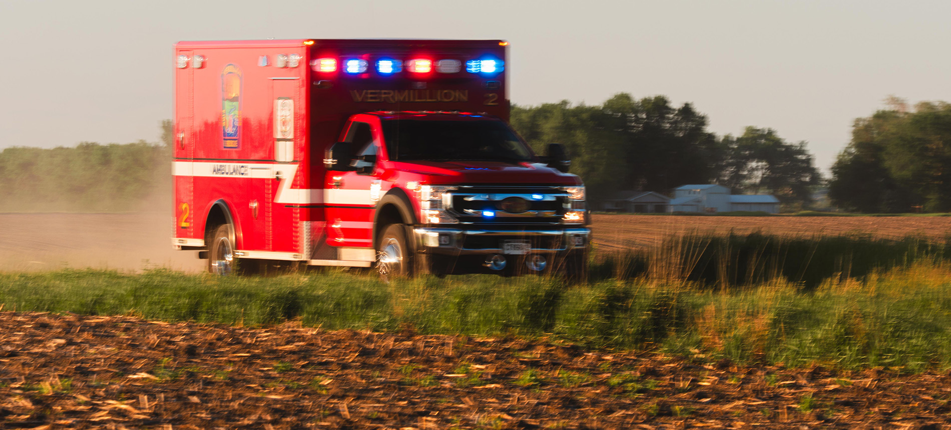 A red ambulance with flashing lights driving down a gravel road in rural South Dakota