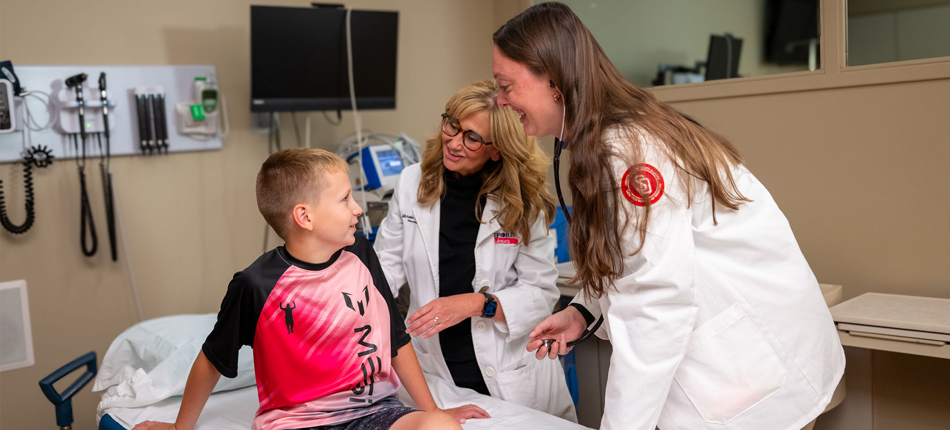 Child at a doctors office laughing with a student nurse and a faculty member