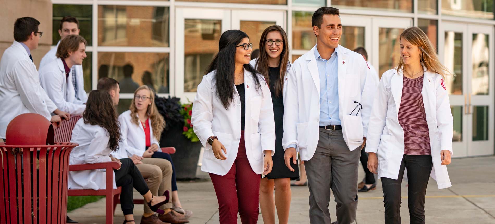 Group of Medical Students in White Coats Walking Outside of Building