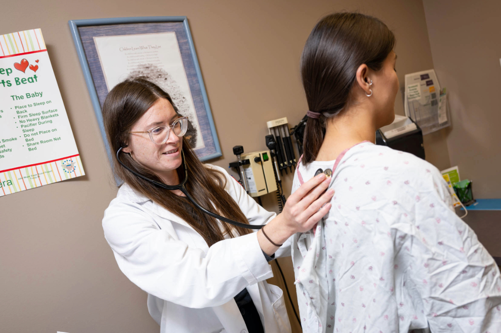A med student in her office feeling the back of a patient in a gown.