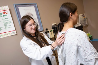 A med student in her office feeling the back of a patient in a gown.