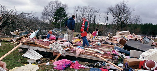 Two people cleaning up a broken house outside.