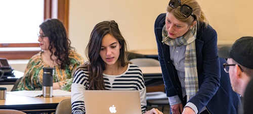 A teacher helping a student with her homework on her laptop.