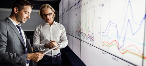 Two businessmen in front of a chart analyzing numbers.