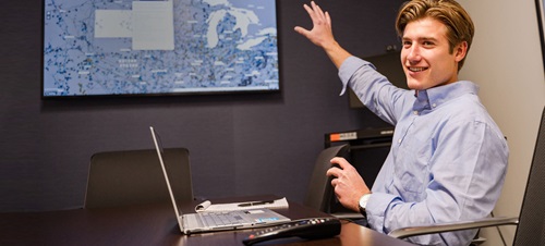 A business student smiling in class pointing at a digital presentation.