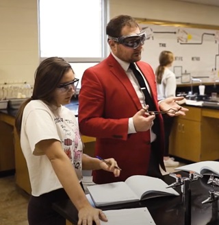 A teacher and a student doing lab work with goggles on.