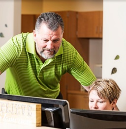 A man looking over a woman's shoulder at her computer.