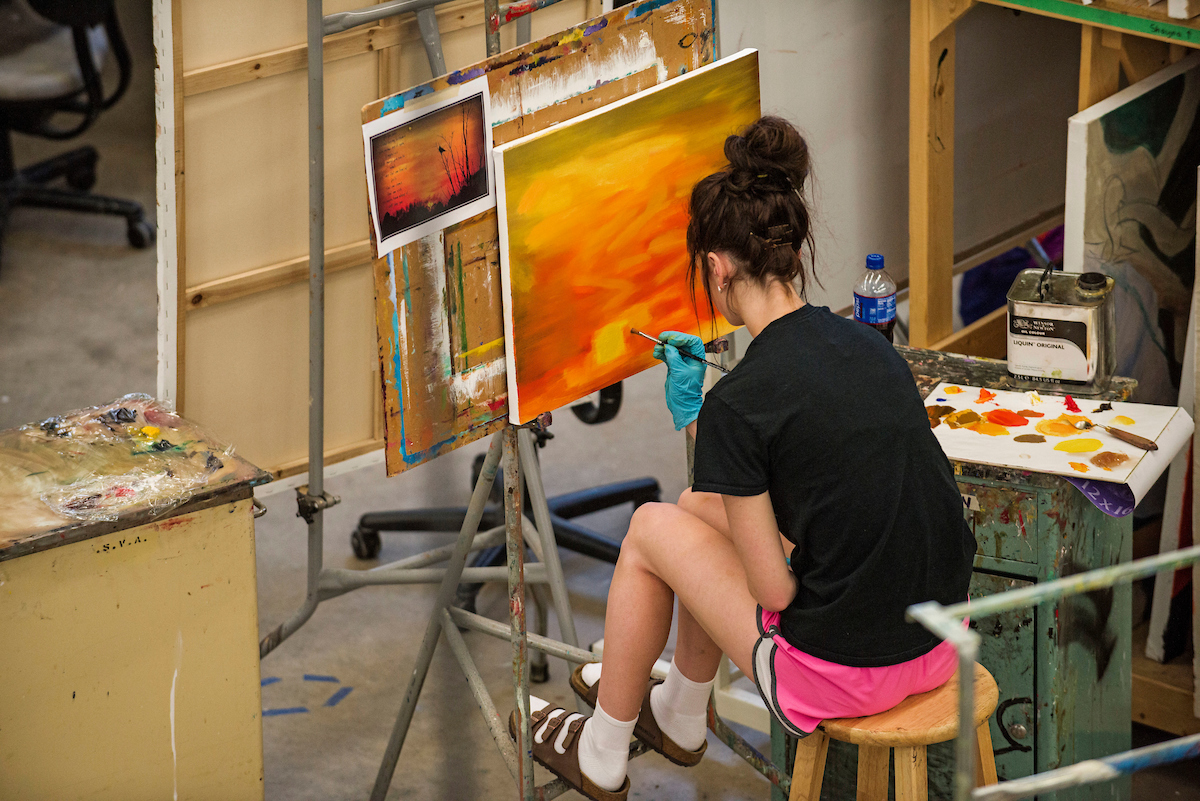 Student painting a sunrise on a canvas