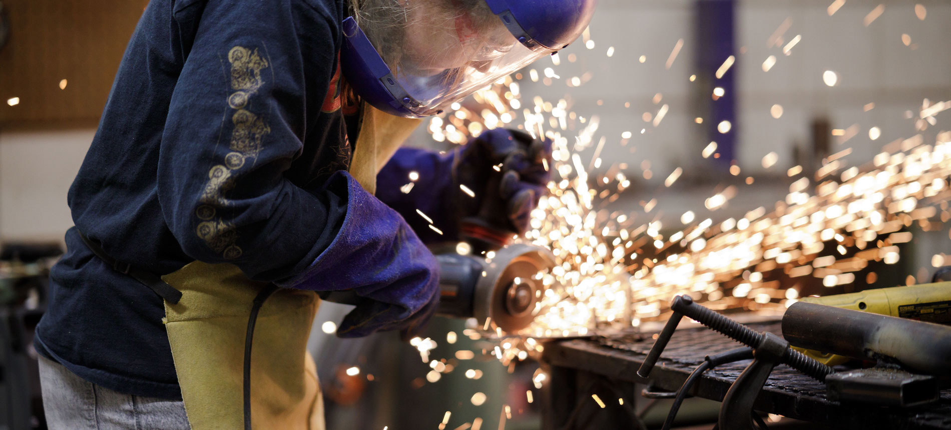 Student working with the theatre set cutting sheet metal with an angle grinder, sparks are flying