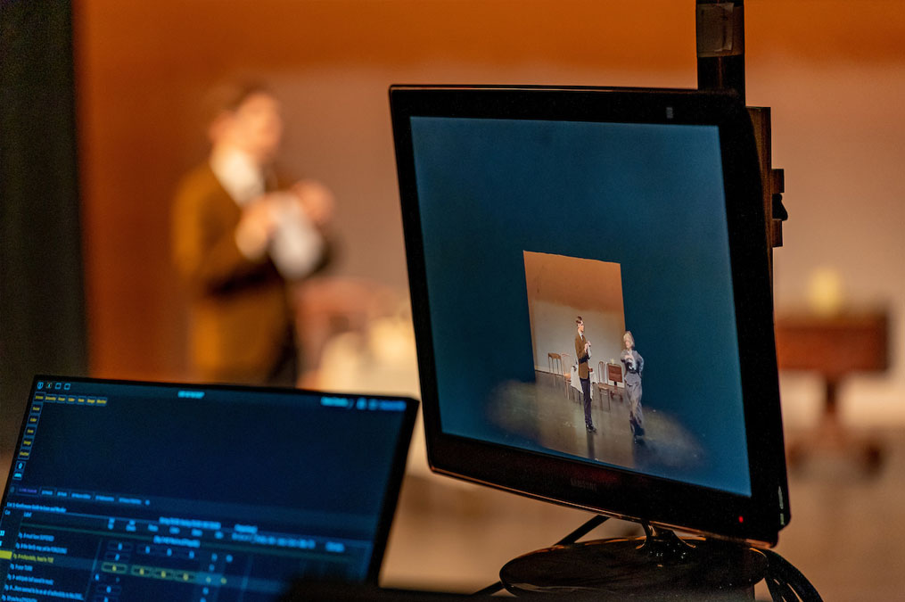 Photo of computer screen showing a live video feed of the live play on stage
