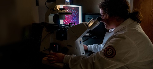 A student looking into a microscope in a dark lab.