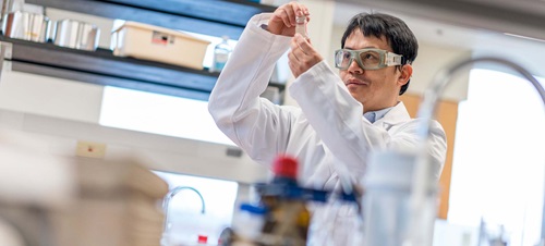 Male in White Lab Coat and Goggles Inside a Research Lab.