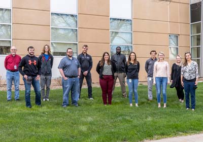 Group of Students with Faculty Members Standing Outside Building.