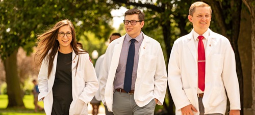 Three Med Students in White Lab Coats Walking Outdoors.