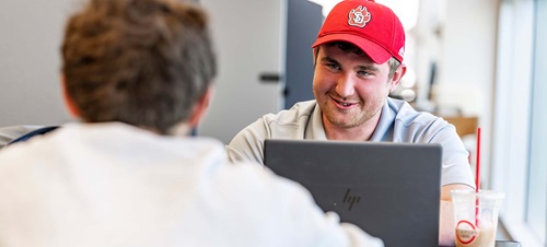 Student smiling, working on computer with coffee.
