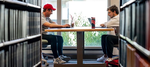 Two Male Students Sitting at Table in the Library.