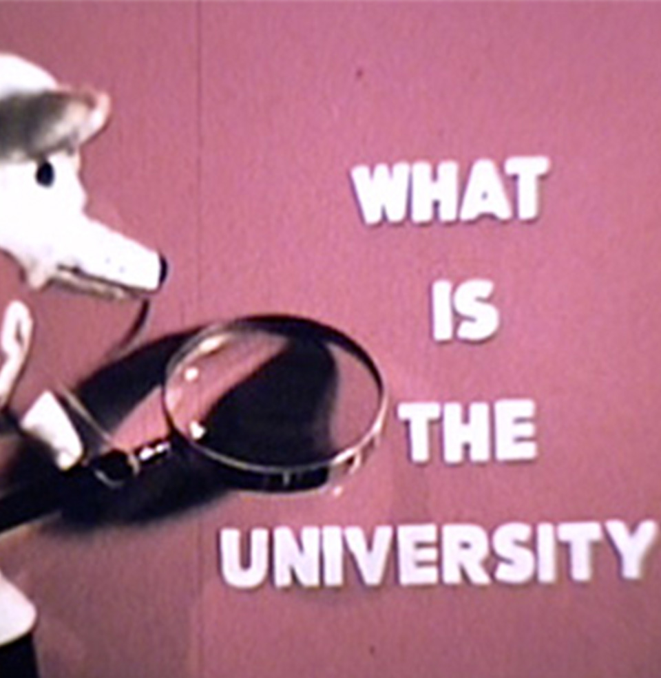 archived photo of charlie holding a magnifying glass looking at the words what is a university