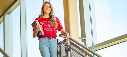 Female Student Walking Down Stairs Carrying a Textbook