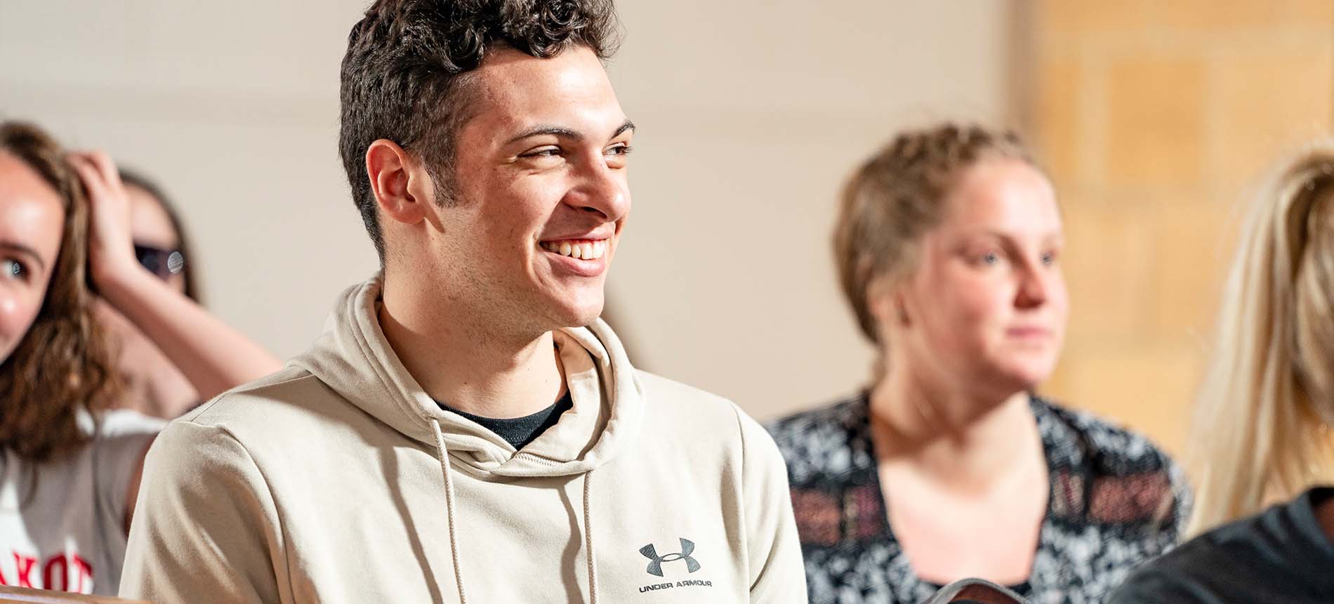 Man smiles in a classroom with other students.
